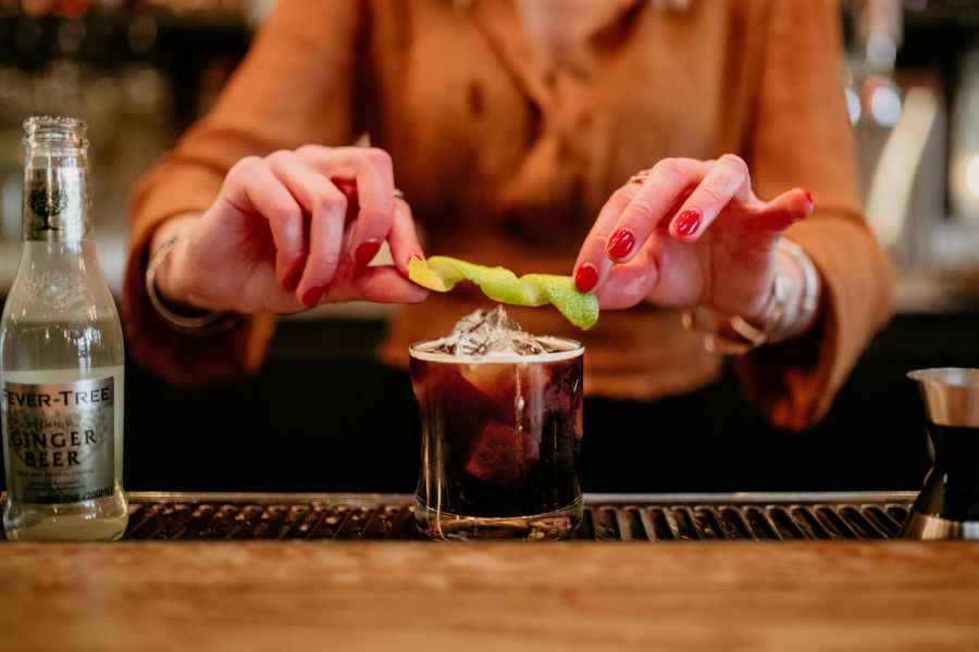 Bartender preparing a drink by twisting a lime above a dark drink