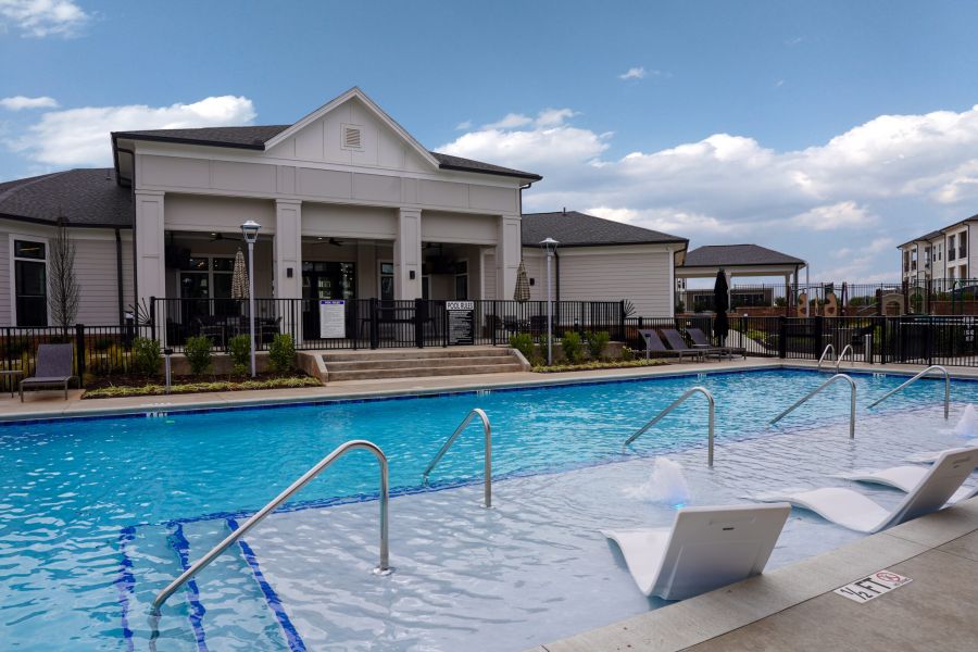 Two children, one girl in a purple swimsuit and one boy in blue shorts, hold hands while playing in a shallow pool at The Lodges at Fort Mill.