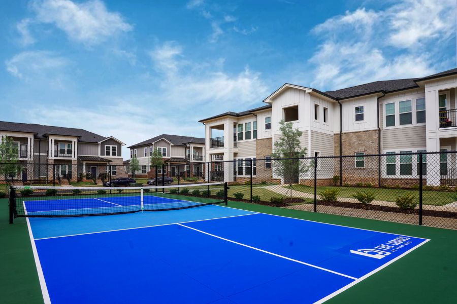 Four people are playing pickleball on an outdoor court at The Lodges at Fort Mill. A man in the foreground is getting ready to hit the ball.