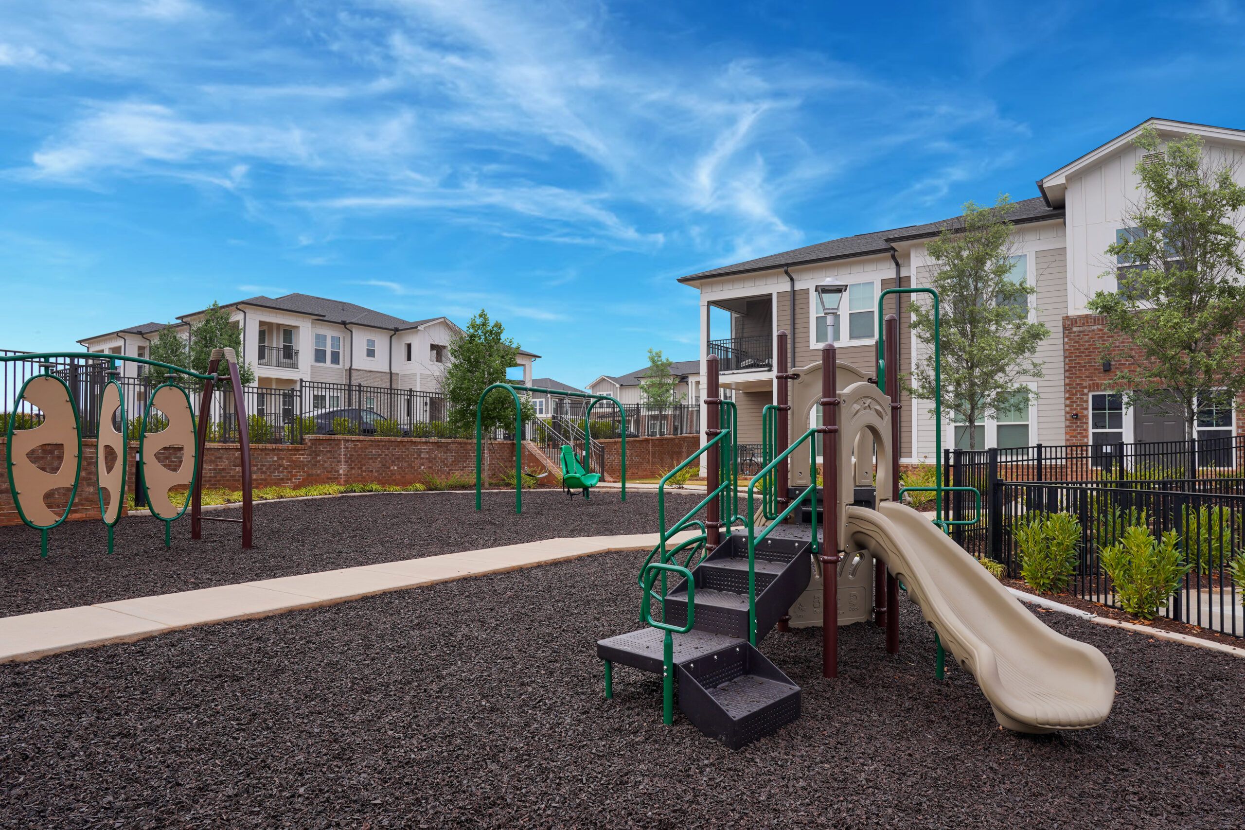 The wooden dock at The Lodges at Fort Mill extends over a calm lake surrounded by lush greenery; a bench is situated on the grassy shore.