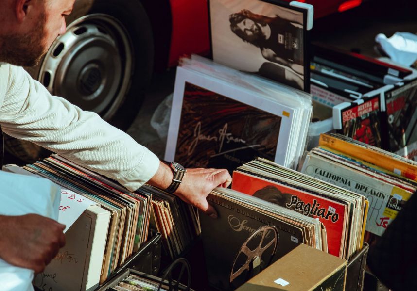 A person flips through crates of vinyl records at an outdoor market, with various album covers visible in the bins.