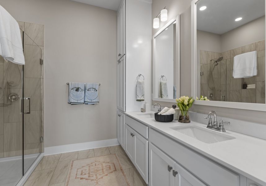 A modern bathroom featuring a double vanity, a glass-enclosed shower, and neutral tile flooring.