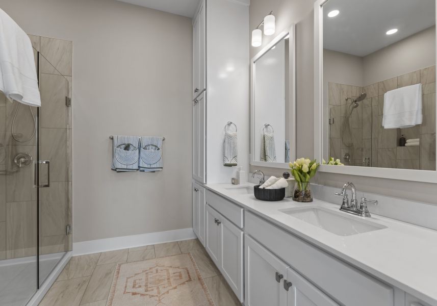 spacious bathroom with a walk-in shower and two sinks with spacious quartz countertops and white cabinetry.