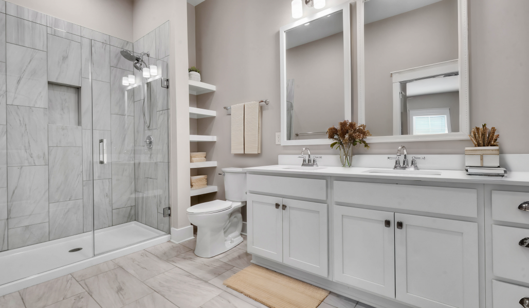 Modern bathroom with a glass shower, double sink vanity, toilet, shelves with towels, and neutral-colored decor.