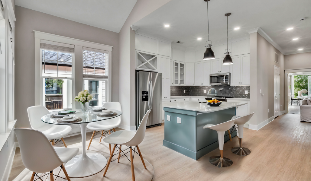 Modern kitchen with a central island, bar stools, stainless steel appliances, and a round dining table set for four near large windows.