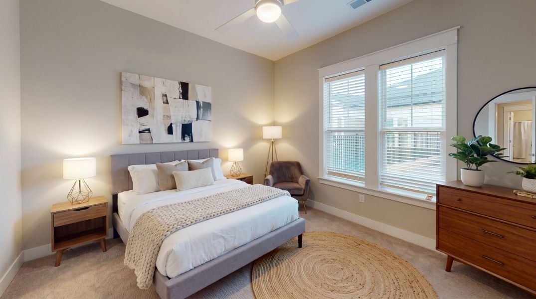 Modern bedroom with a bed, two nightstands, lamps, a chair, dresser with a mirror, large window, and abstract wall art.