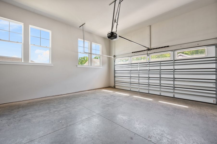 Empty two-car garage with concrete floor, white walls, three windows, and a closed segmented garage door with an automatic opener.