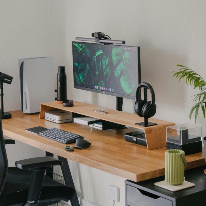 A modern desk setup with a monitor, keyboard, mouse, headphones, plant, and office accessories on a wooden desk.