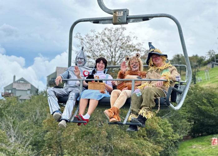 Four people in Wizard of Oz costumes ride a ski lift; one is dressed as the Tin Man, another as Dorothy, the third as the Cowardly Lion, and the fourth as the Scarecrow. It's a whimsical scene you might encounter at Lodges at Fort Mill.